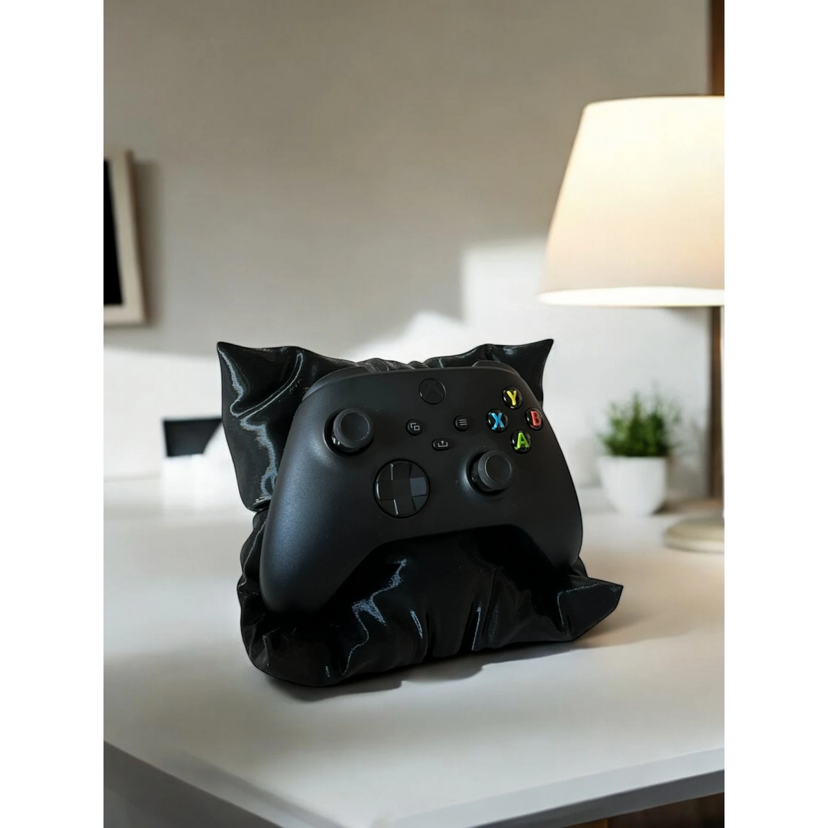 Black pillow-shaped stand holding an Xbox controller, ideal for gaming setups.
