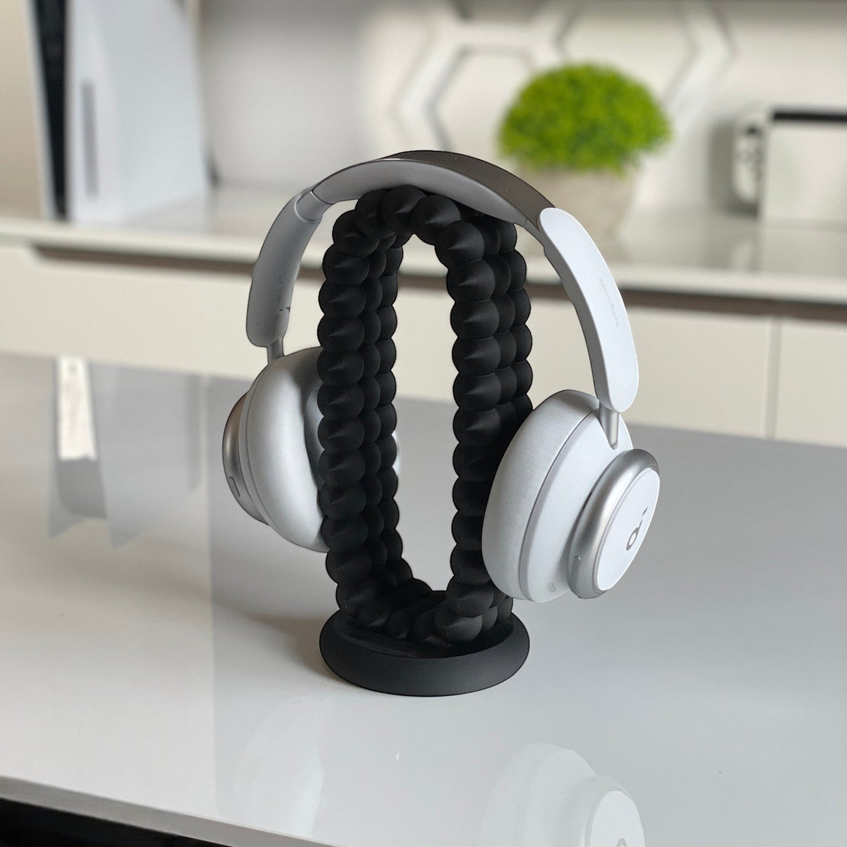 Magicland 3D black flexible headphone stand holding white over-ear headphones on a white desk.