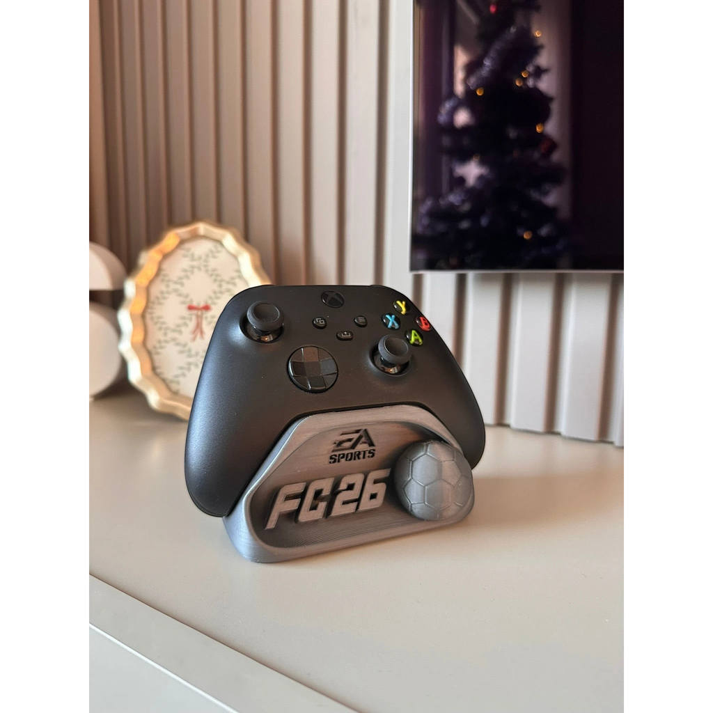Magicland 3D FC26 kol tutucu stant, Xbox oyun kumandası için tasarlanmış, üzerinde EA Sports logosu ve futbol topu detayı bulunan gri renkli bir aksesuardır.