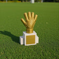 Magicland 3D altın eldiven futbol ödülü, beyaz kaide üzerinde duruyor. Yapay çim zeminde gölgeli.