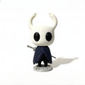 Magicland 3D Hollow Knight figürü, beyaz boynuzlu, siyah gözlü ve lacivert pelerinli, kılıcı elinde tutuyor.