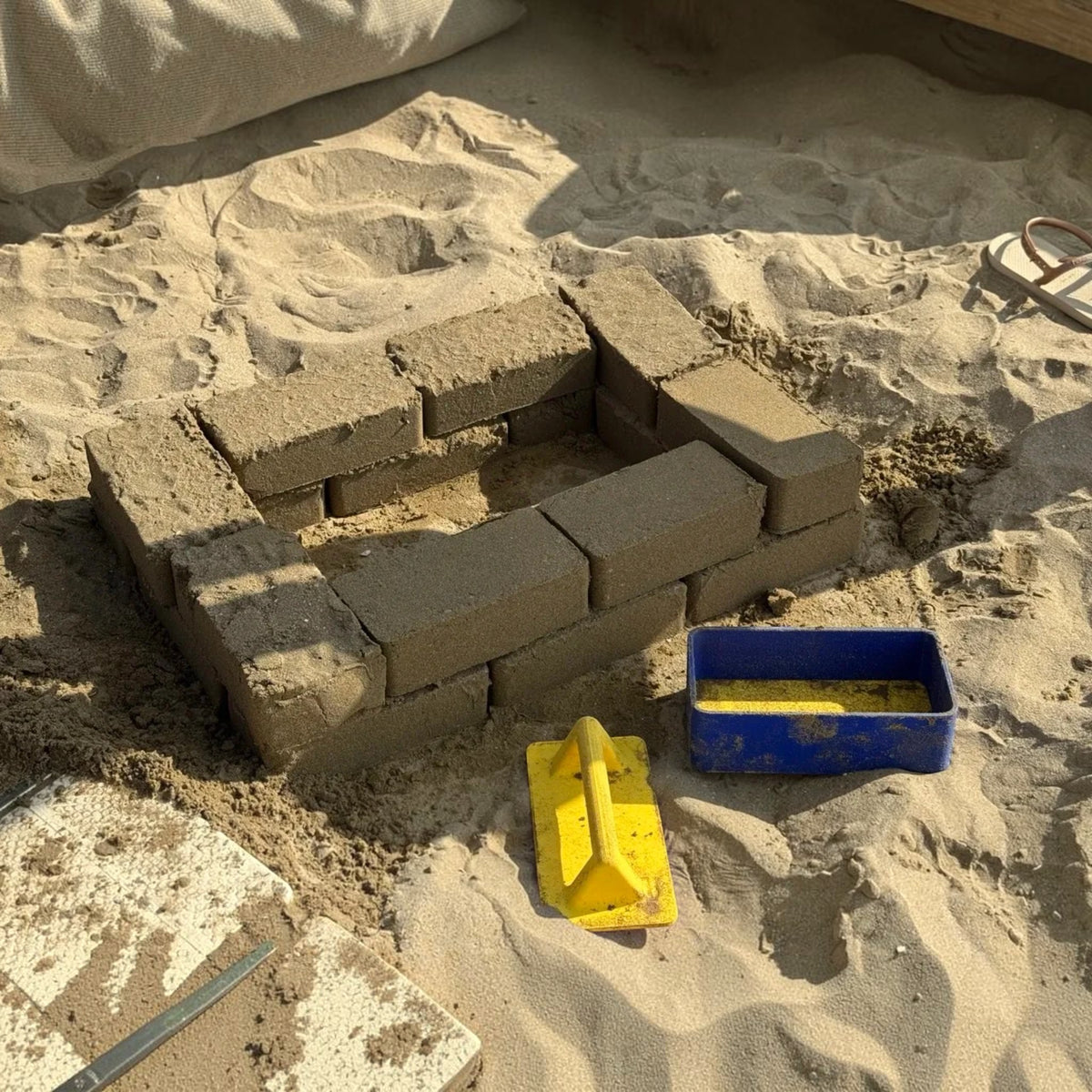Magicland 3D kum kalesi tuğla kalıbı seti ile plajda inşa edilmiş kumdan duvar ve sarı bastırma aparatı