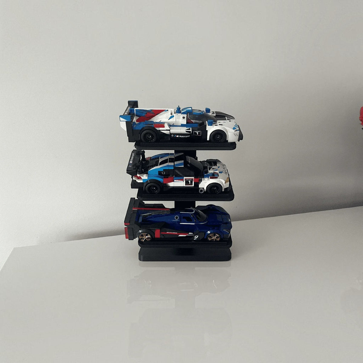 Magicland 3D siyah üç katlı dikey Lego Speed Champions araç sergileme standı üzerinde üç adet yarış arabası modeli.