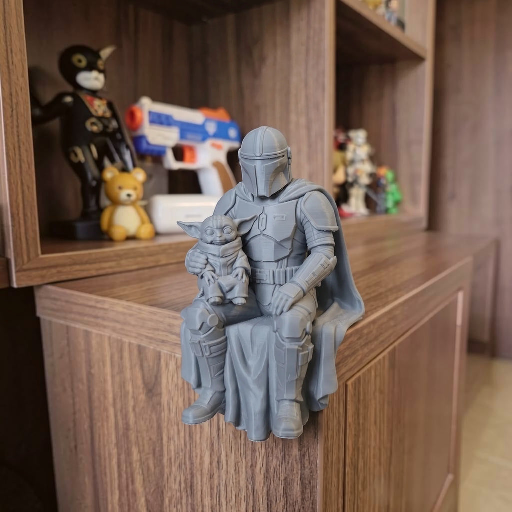Magicland 3D tasarımı gri PLA malzemeden üretilmiş, raf kenarında oturan Mandalorian ve Grogu figürü.