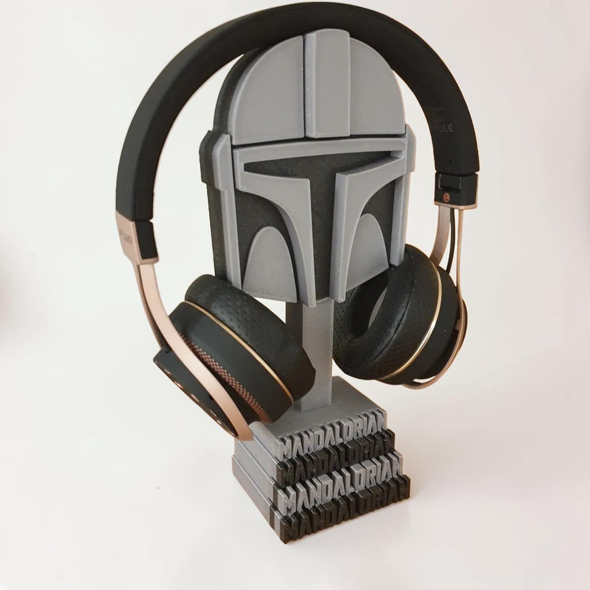Magicland 3D Mandalorian helmet headphone stand in grey, holding black and rose gold headphones.