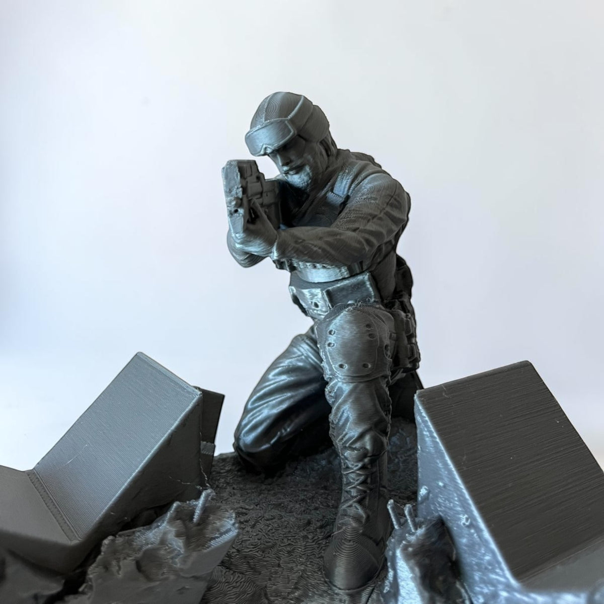 Magicland 3D grey soldier figurine holding a weapon, kneeling on a textured base with debris.