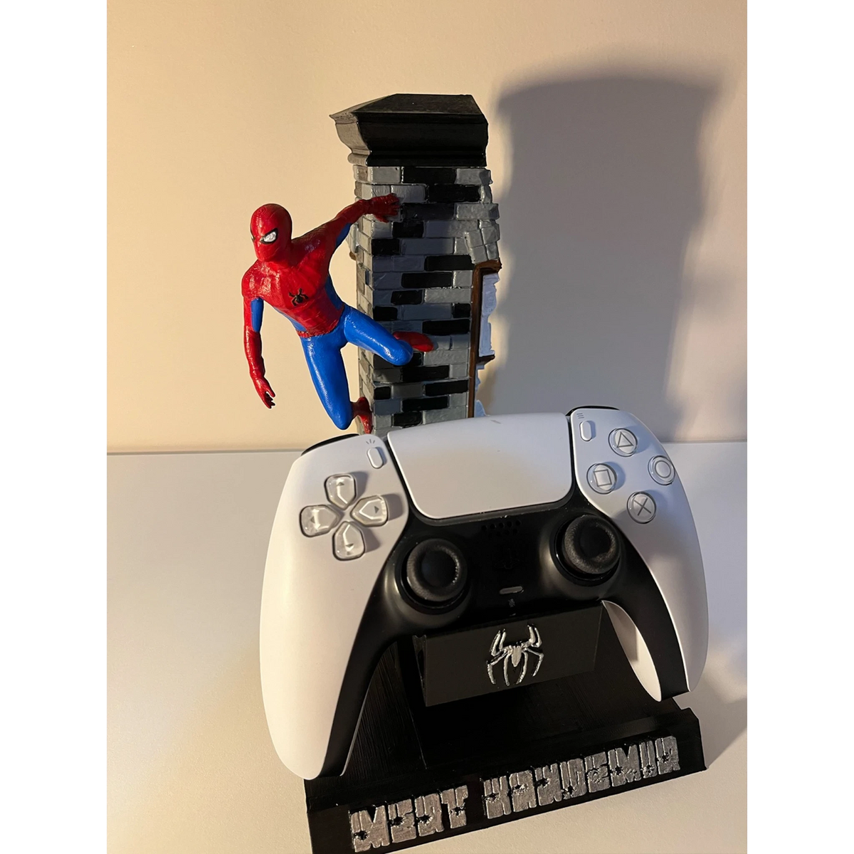 Magicland 3D Spiderman temalı özel tasarım PS5 kontrolcü standı. Kırmızı ve mavi kostümlü Spiderman figürü, tuğla desenli bir binanın üzerinde duruyor.