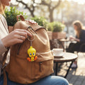 Magicland 3D sarı Tweety anahtarlık, kahverengi sırt çantasına takılı, dış mekan kafe ortamı.