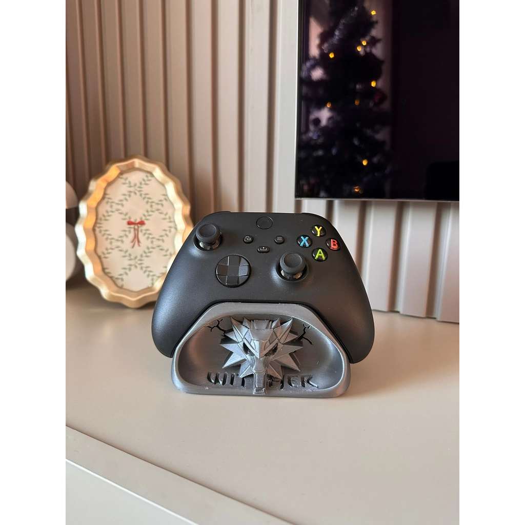 Magicland 3D Witcher temalı gri renkli oyun kumandası tutucu stant. Witcher logosu ve yazı detayı bulunur.