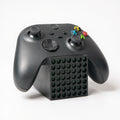 Black Xbox Series X controller resting on a black stand designed to look like a mini Xbox Series X console.