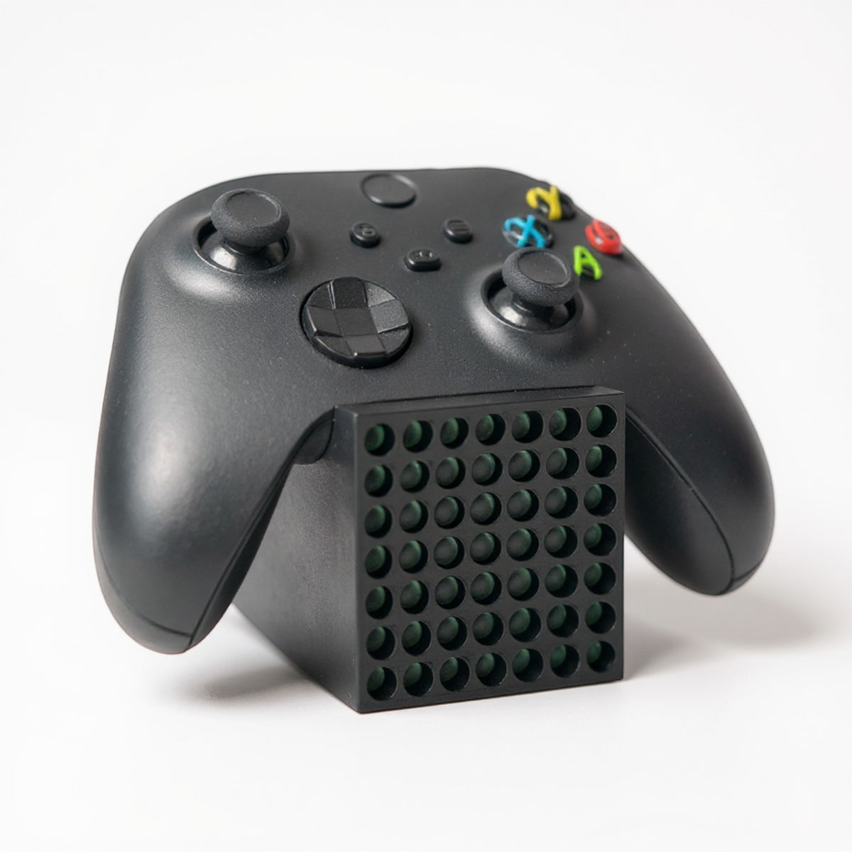 Black Xbox Series X controller resting on a black stand designed to look like a mini Xbox Series X console.