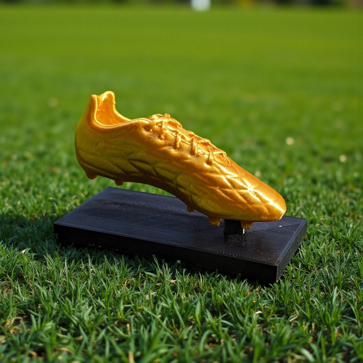 Magicland 3D altın futbol ayakkabısı ödülü, siyah bir kaide üzerinde, çim zeminde duruyor.