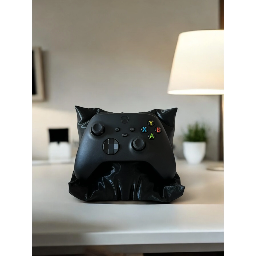 Black Xbox controller resting on a black pillow-shaped stand, a decorative accessory for gaming setups.
