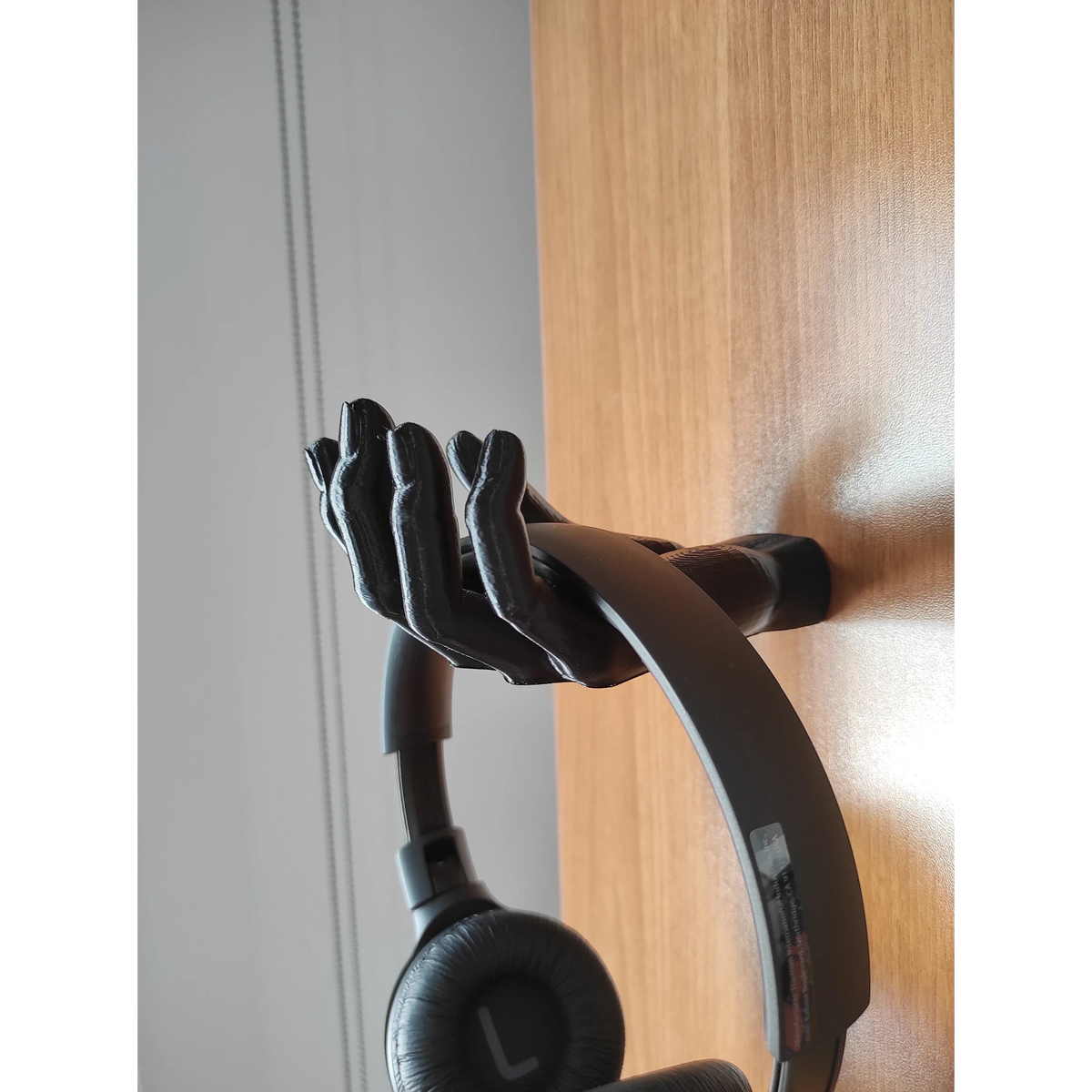 Magicland 3D black hand-shaped headphone stand holding black headphones on a wooden surface.