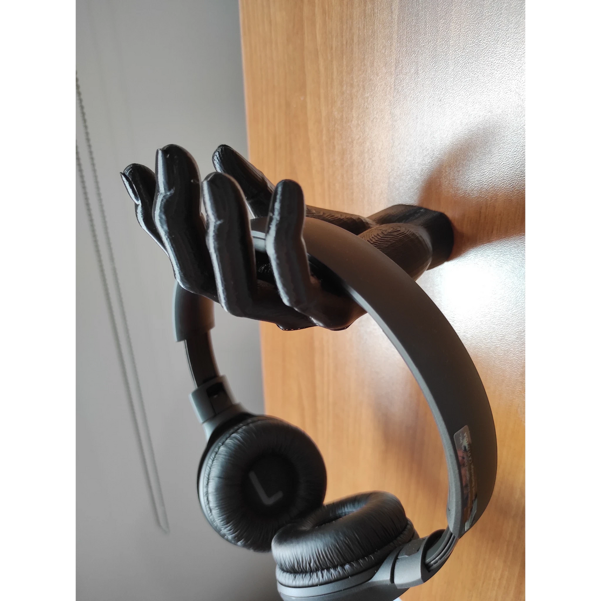 Black 3D printed hand-shaped headphone stand holding black headphones. Unique desk accessory.