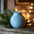 Magicland 3D light blue ceramic vase with embossed snowflake pattern, next to pine branches and bokeh lights.