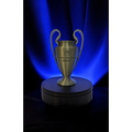 Magicland 3D replica of the Champions League trophy, a metallic gold cup with two handles on a rotating black stand against a blue backdrop.