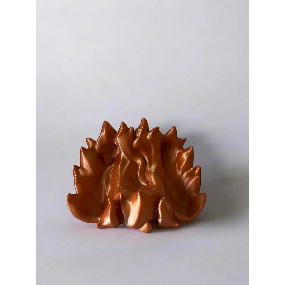 Magicland 3D copper flame-themed phone stand with a metallic sheen, designed to hold a phone upright.
