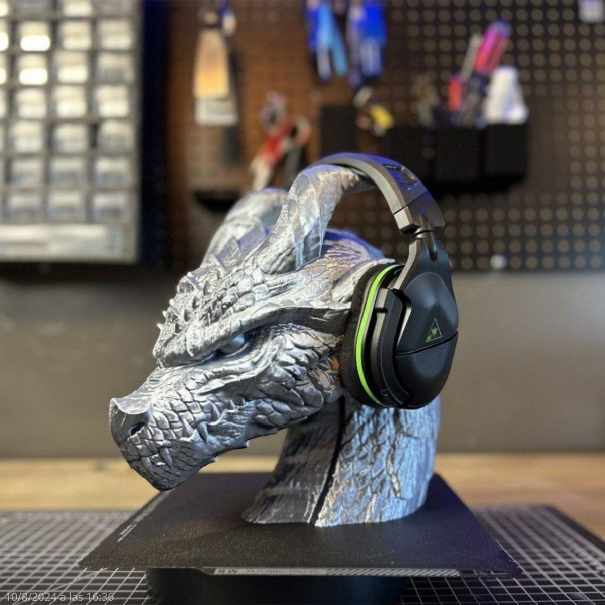 Magicland 3D silver dragon head headphone stand, detailed scales, holding black gaming headset with green accents.
