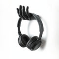 Black 3D printed hand-shaped headphone stand by Magicland 3D, mounted on a white wall.