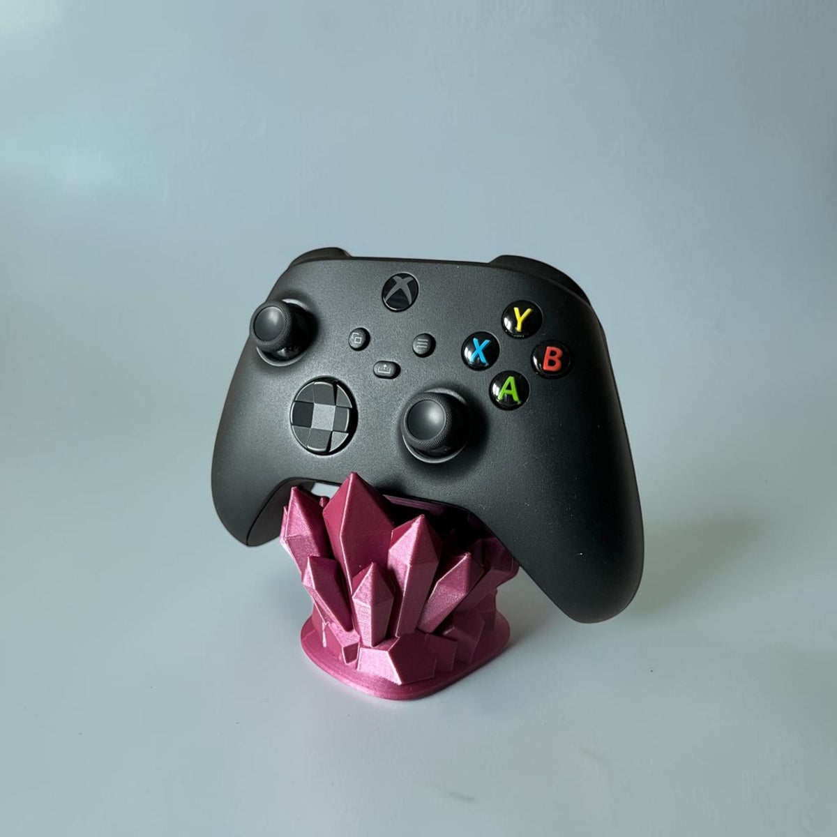 Magicland 3D crystal-shaped controller stand in magenta, holding a black Xbox controller.