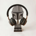 Magicland 3D Mandalorian helmet headphone stand in grey and black, holding black and rose gold headphones.