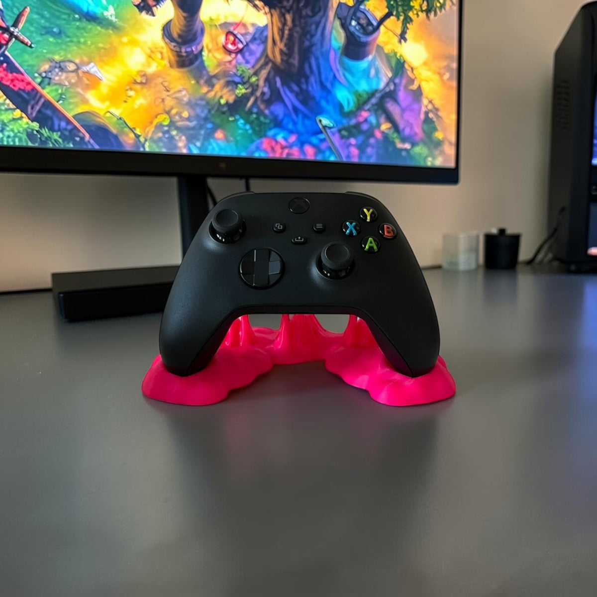 Magicland 3D pink sticky effect controller stand holding a black Xbox controller on a white desk.