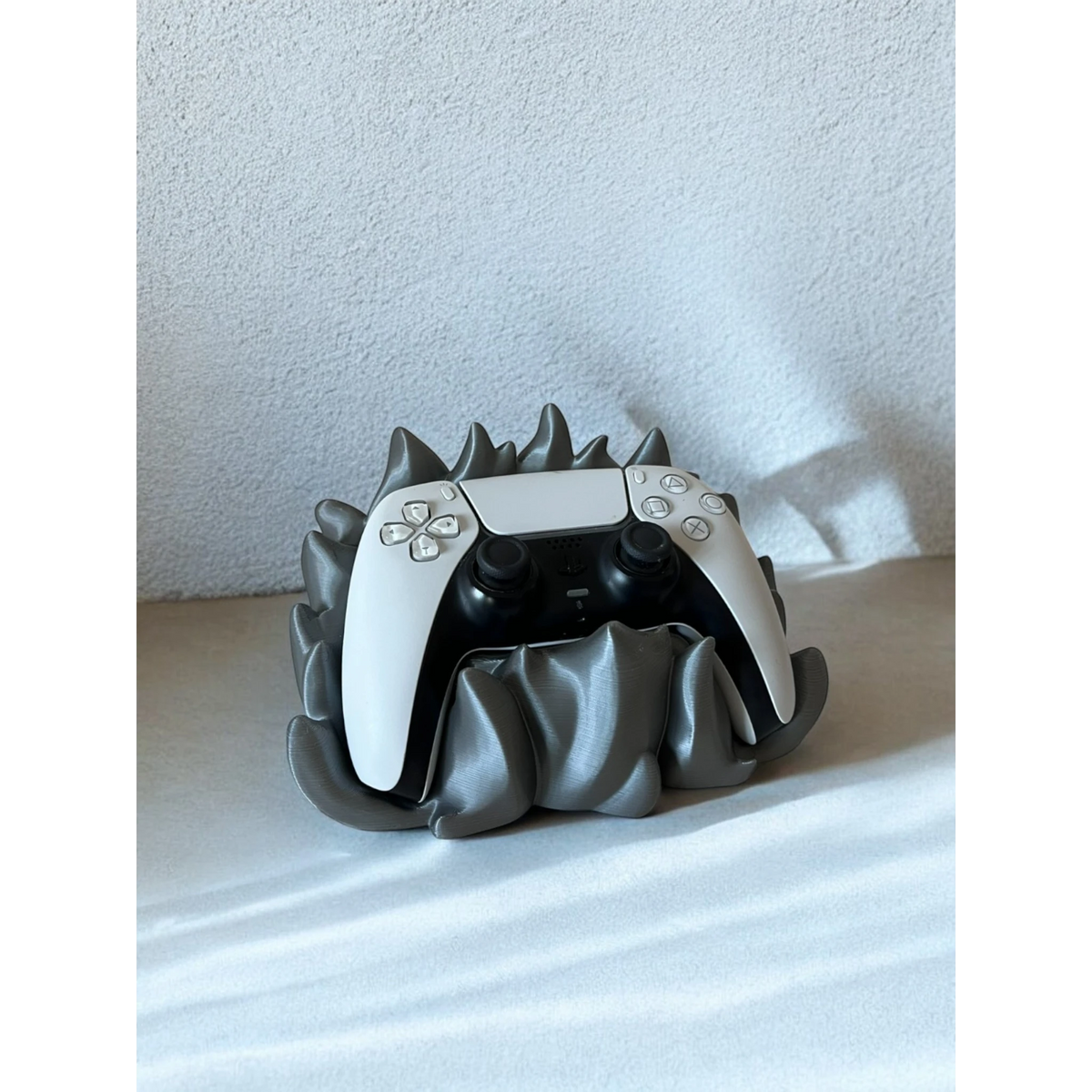 Magicland 3D grey flame-themed stand holding a white PlayStation 5 controller. Unique 3D printed accessory.