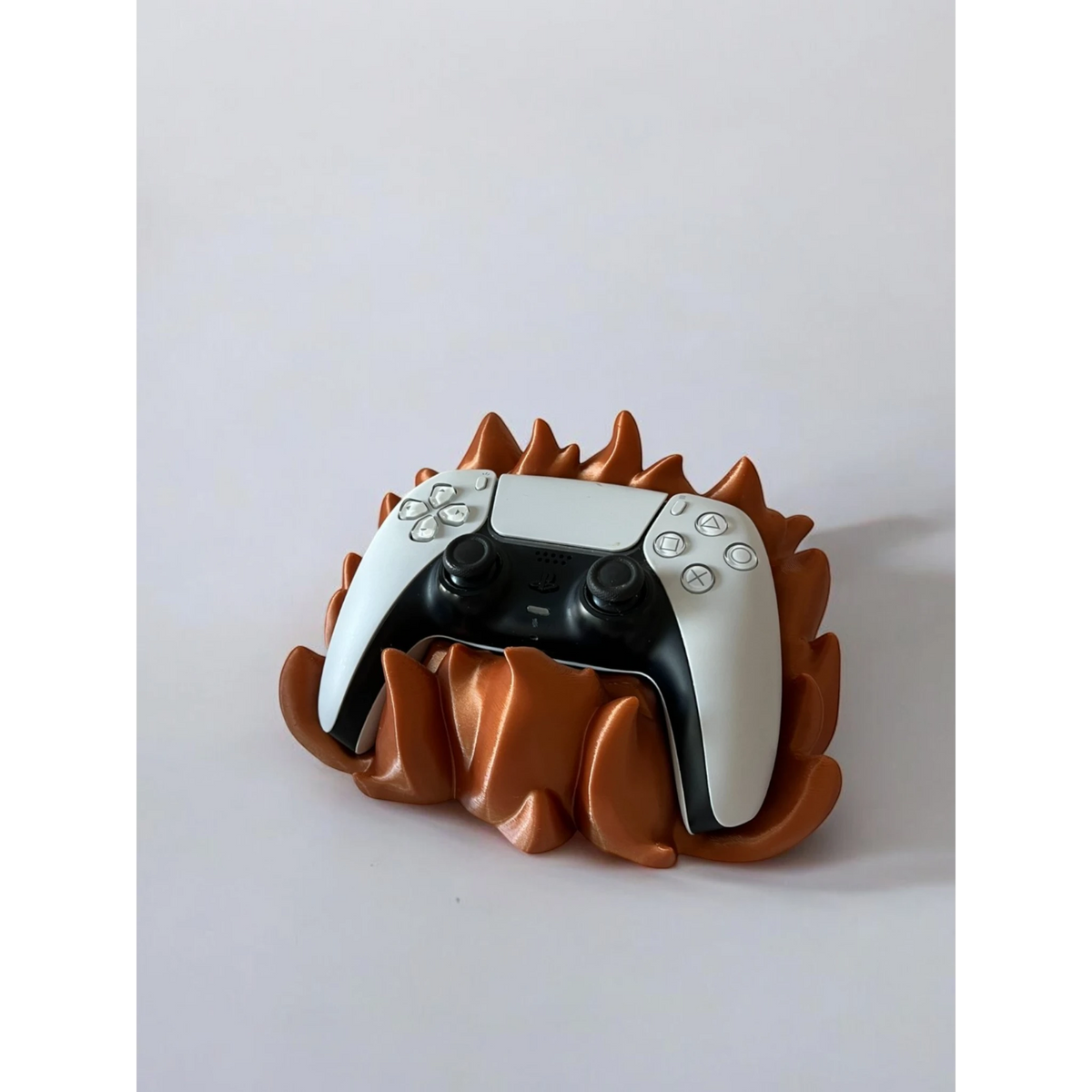 Magicland 3D flame-themed stand holding a white and black PS5 controller. The stand is metallic orange with flame-like sculpted details.