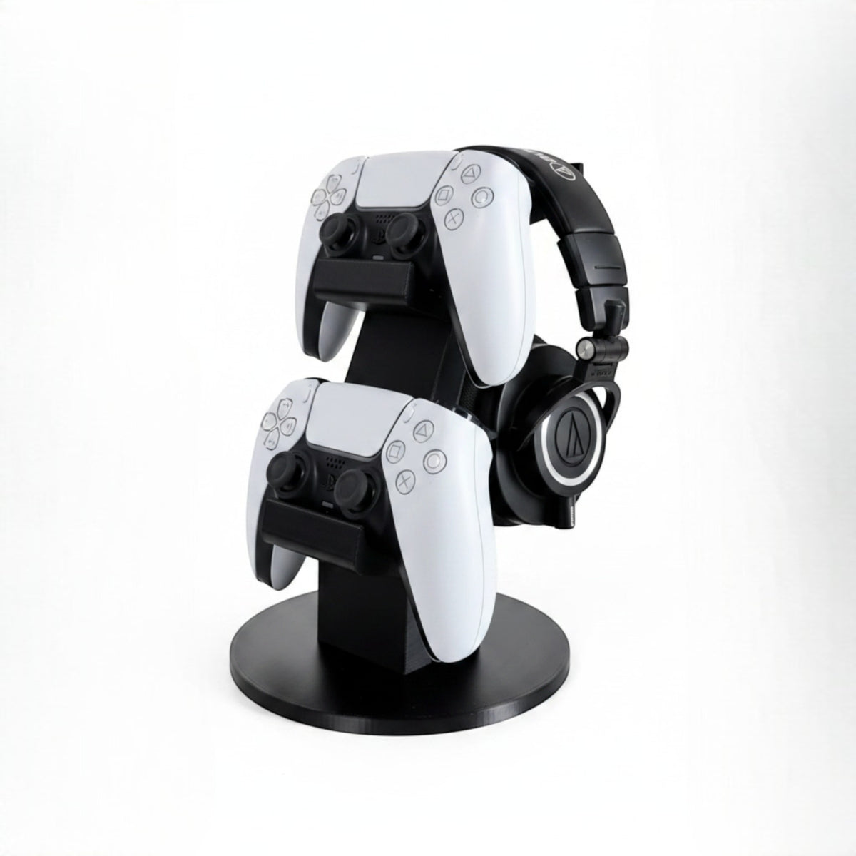 Magicland 3D black stand for two white PS5 controllers and headphones, keeping gaming setup tidy.