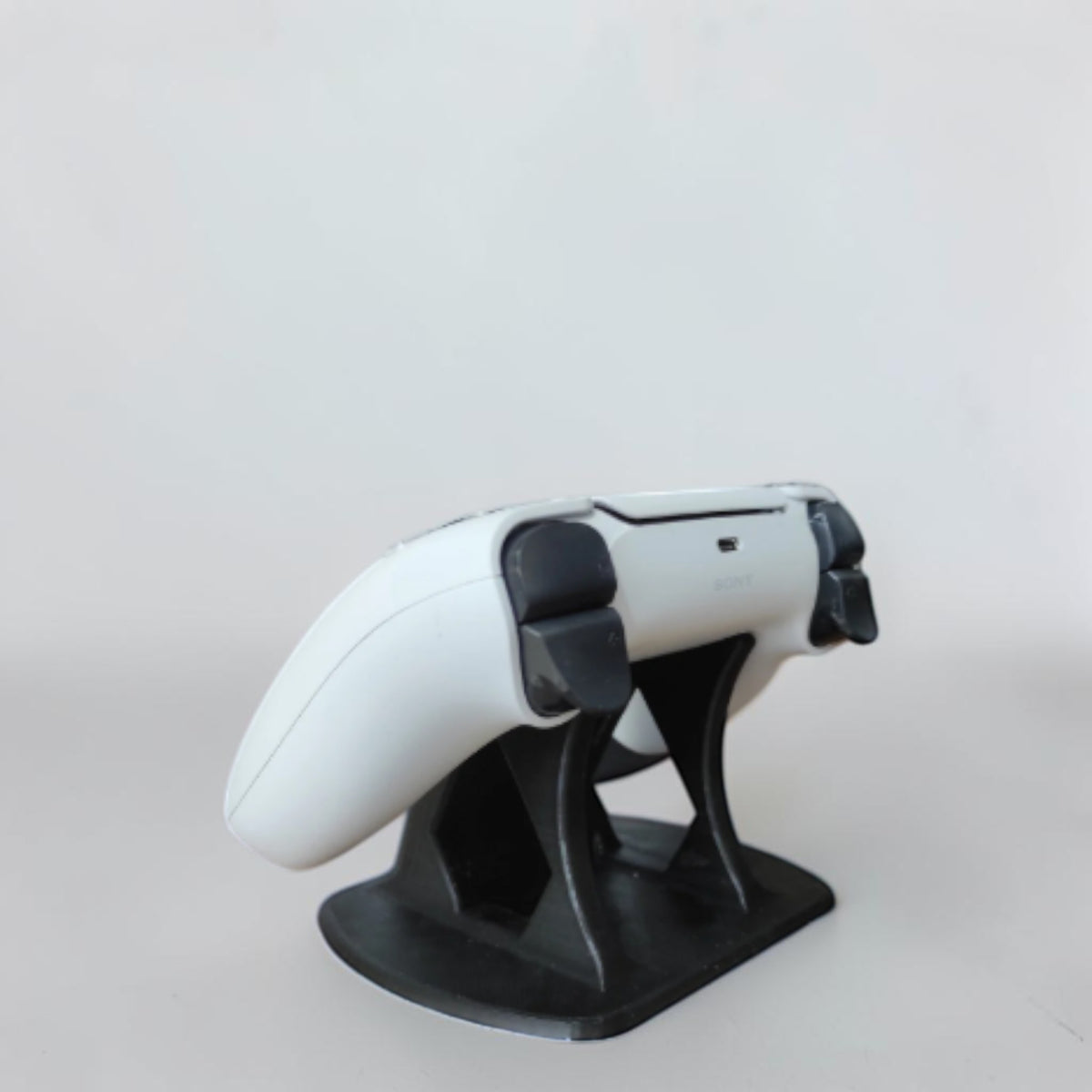 Magicland 3D black PS5 controller stand with PlayStation logo detail, holding a white DualSense controller.