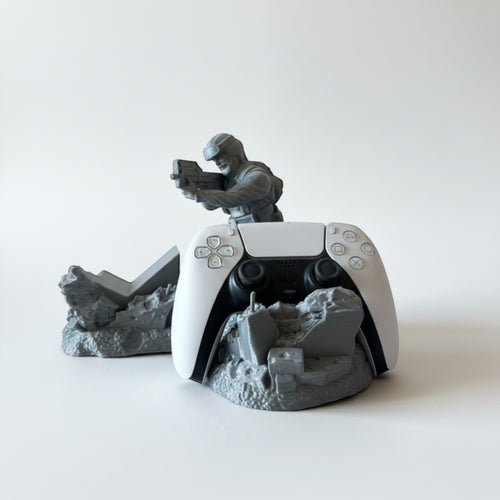 Magicland 3D Asker Figürlü Kol Standı, a grey soldier figure holding a gun, displays a white PS5 controller on a ruined base.