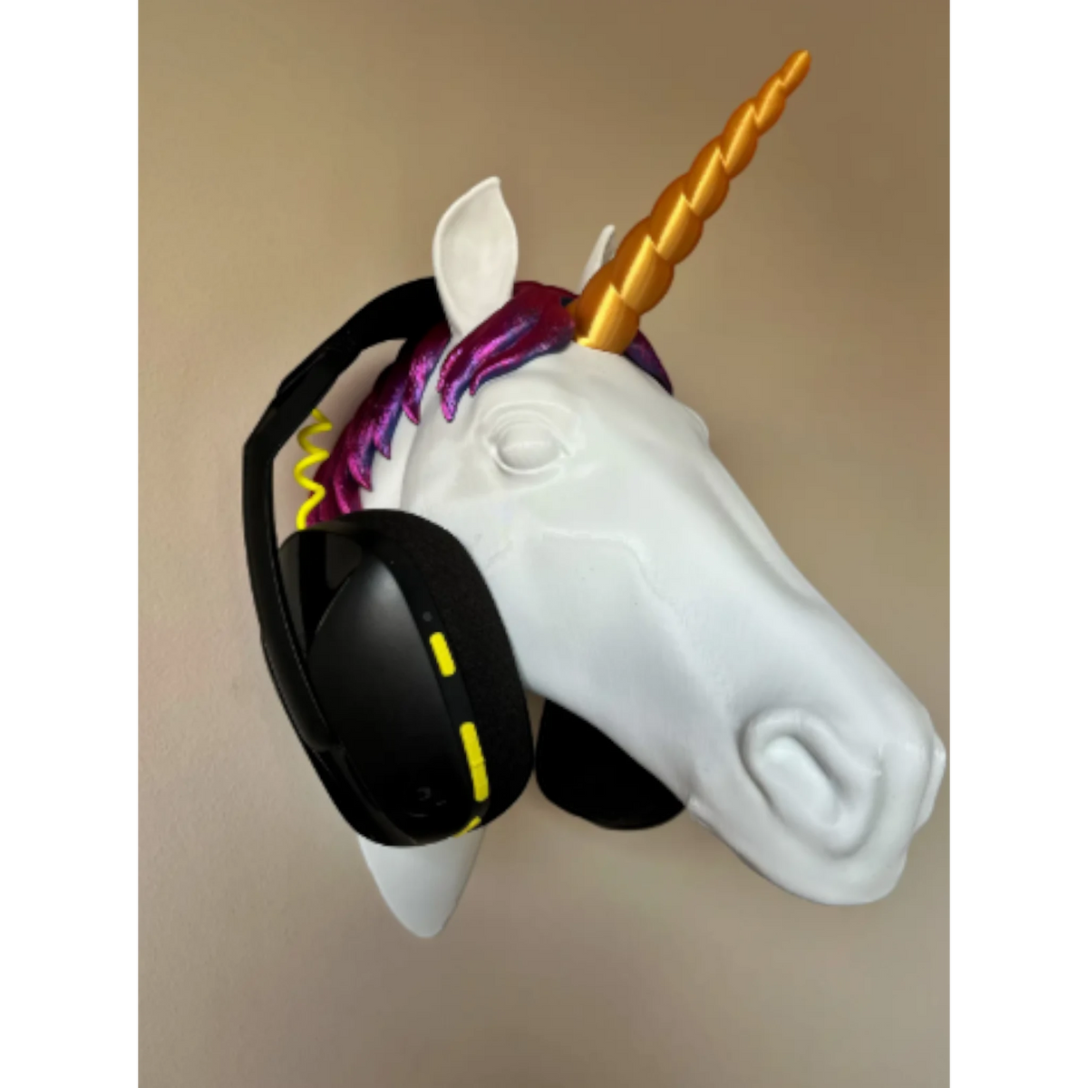 Magicland 3D white unicorn head headphone stand with gold horn and purple mane, holding black headphones.