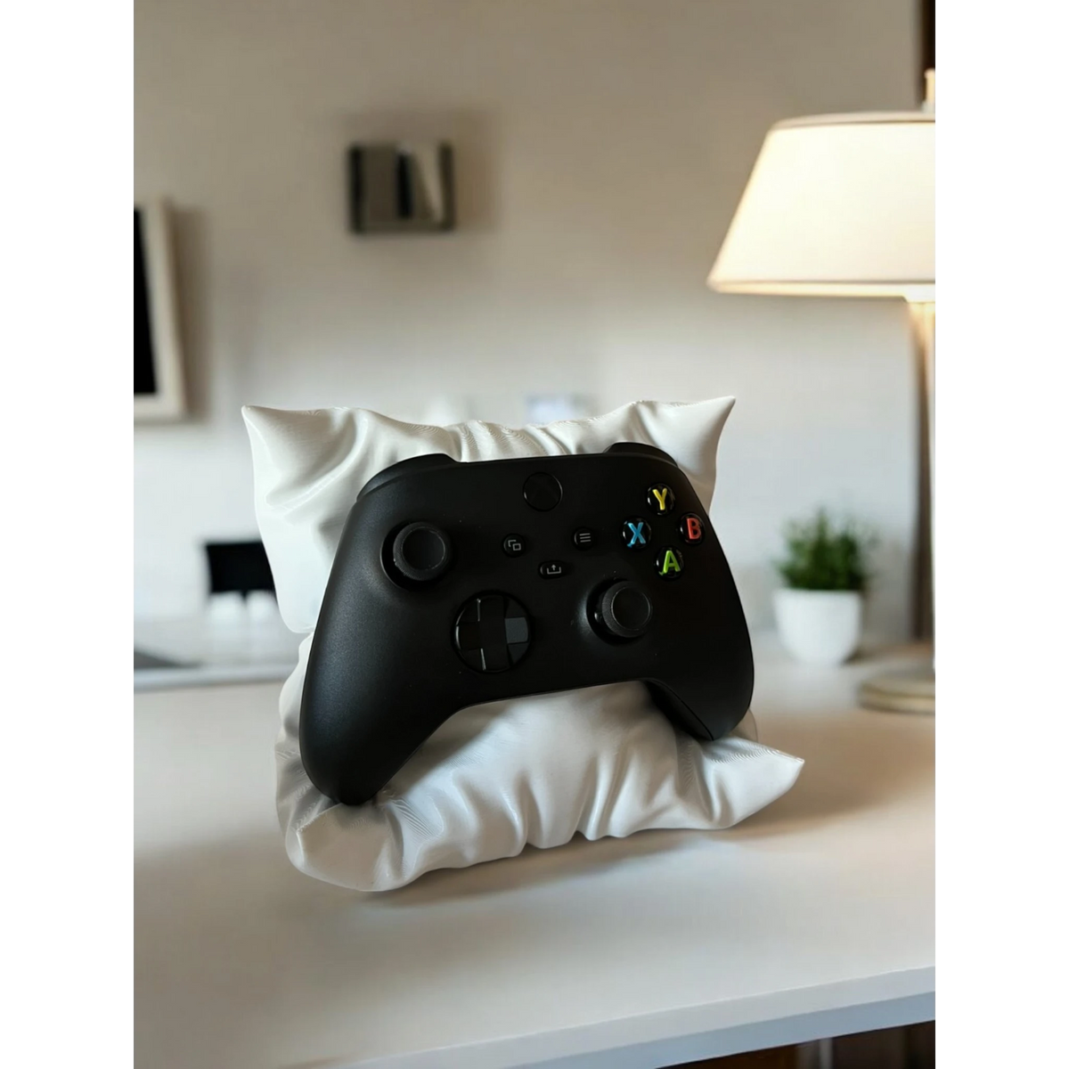 Black video game controller resting on a white decorative pillow stand by Magicland 3D.