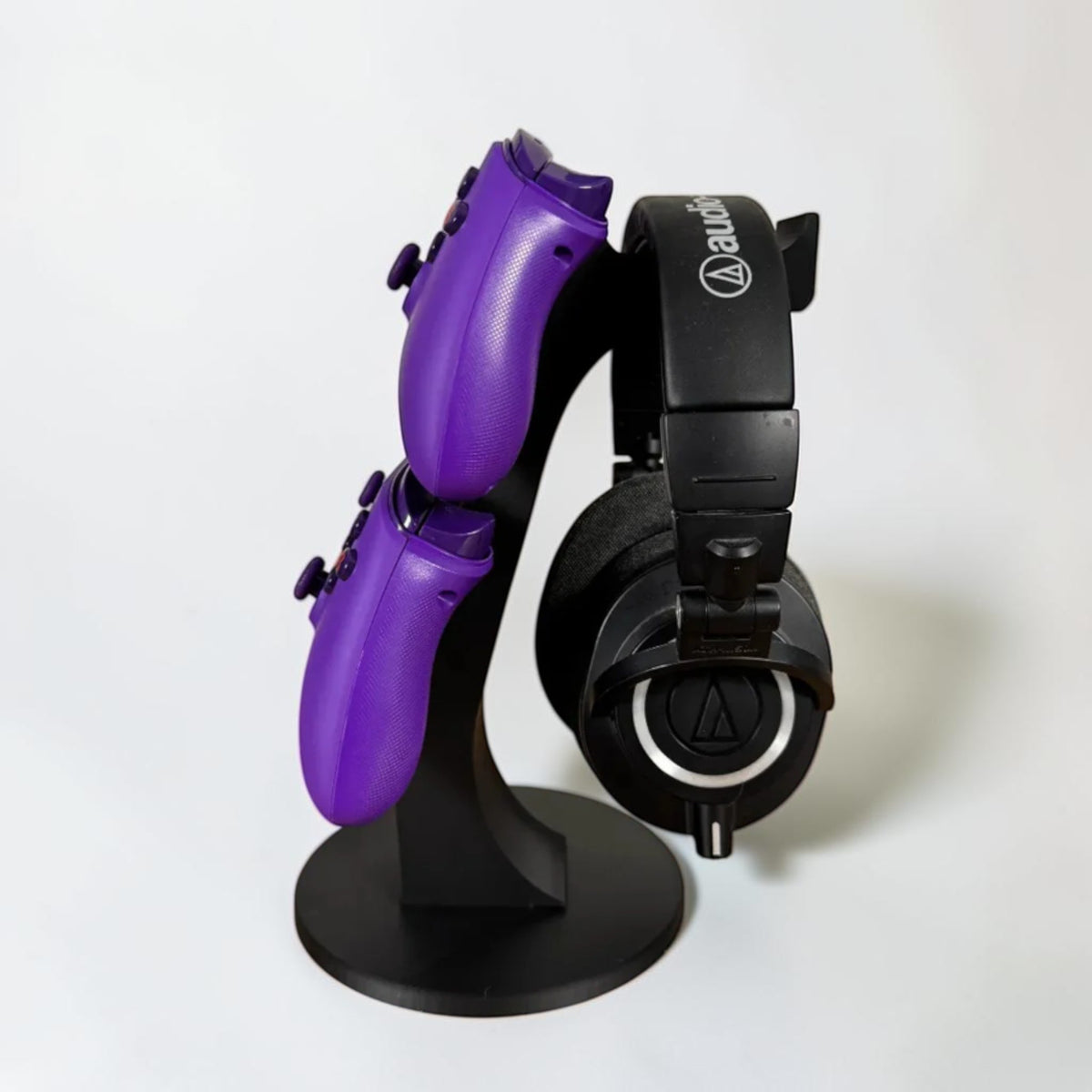 Magicland 3D black stand holding two purple Xbox controllers vertically and a pair of black headphones.