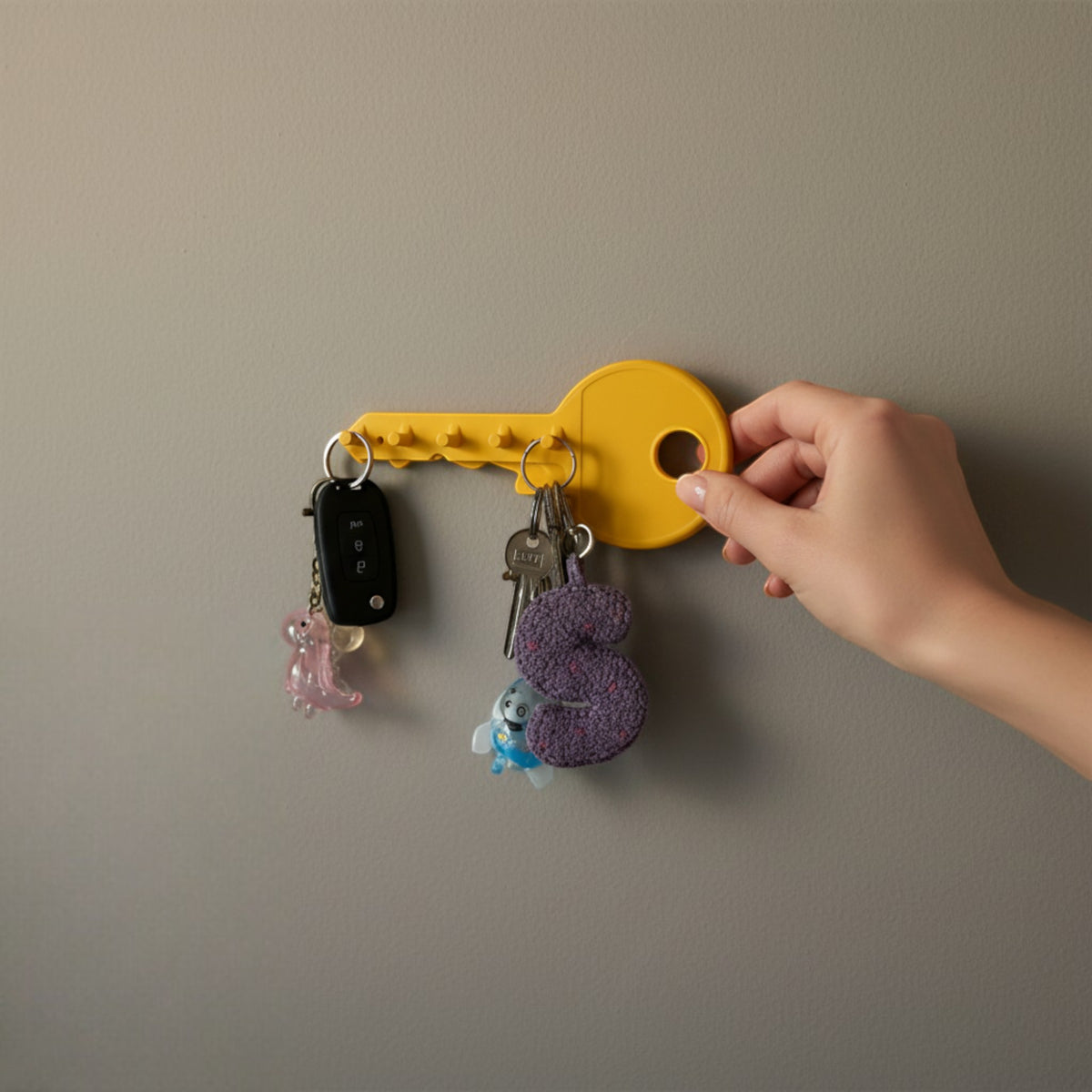 Magicland 3D yellow key-shaped wall hook holding several keys and keychains on a grey wall.